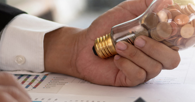 Hand holding a lightbulb with coins inside.